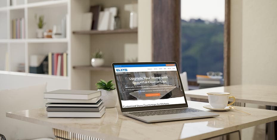 Elite Granite and Tile website on a laptop sitting on a marble countertop