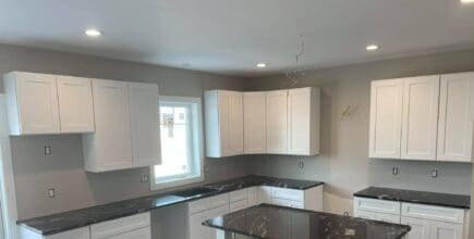 remodeled kitchen with gray walls, white cabinets, and black countertops
