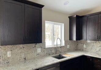 remodeled kitchen with black cabinets and gray countertops/stone backsplash